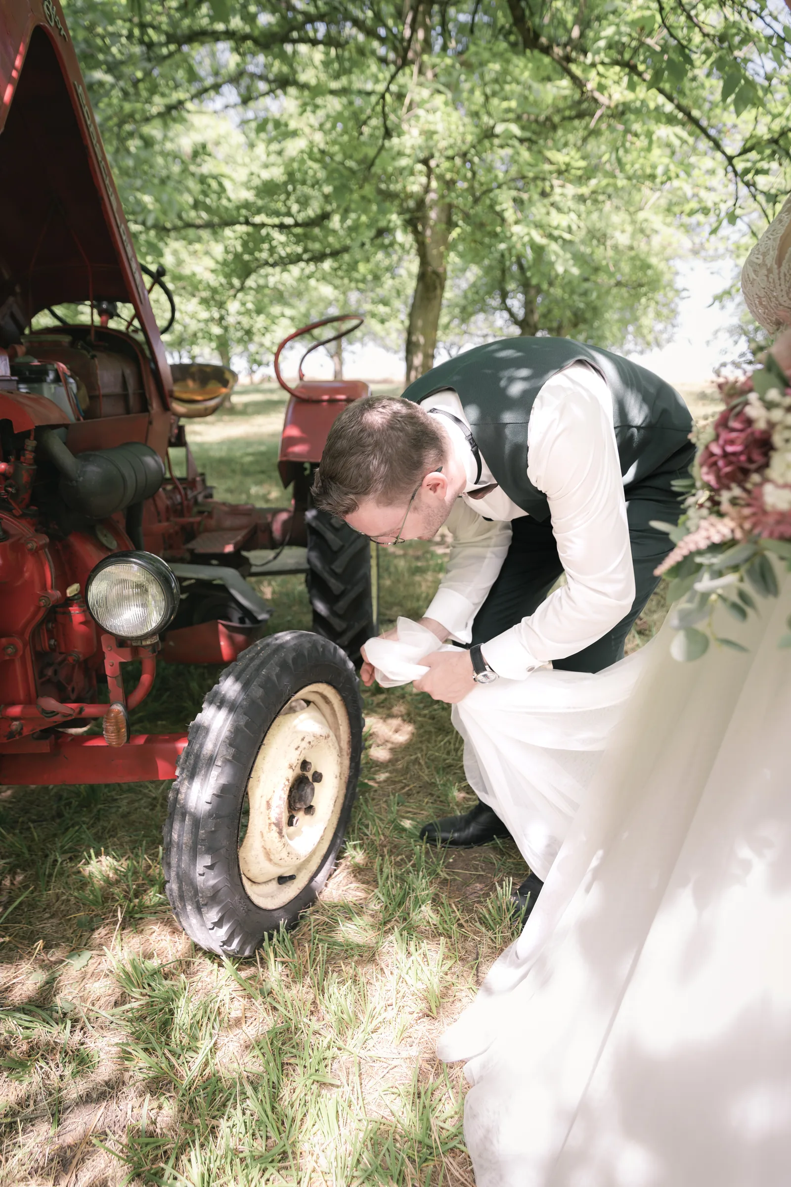 Bräutigam putzt Oldtimer-Traktor mit Brautkleid